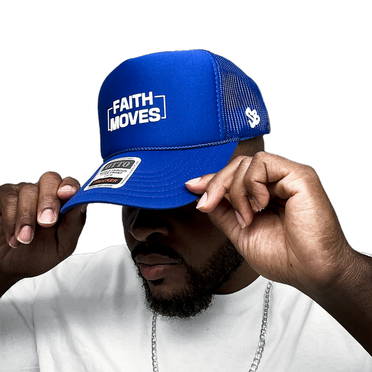 Royal blue Faith Moves trucker hat with white embroidered logo, worn by model adjusting the brim – mesh back and SB logo visible